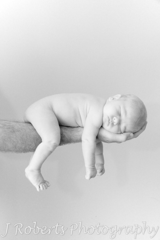 Newborn baby asleep drapped over fathers arm - newborn portrait photography sydney